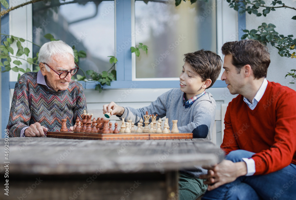 Man looking at father playing chess with son in backyard Man looking at father playing chess with son in backyard
