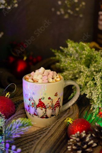 Enchanting holiday setup featuring a mug filled with hot cocoa and marshmallows, adorned with festive chicken illustrations, surrounded by wintery flora and baubles.