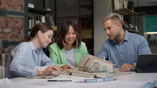 Architects and asian designer working on house layout in office. Diverse group of creative people at desk talking and discussing home design. Specialists looking at detailed projection of mini model