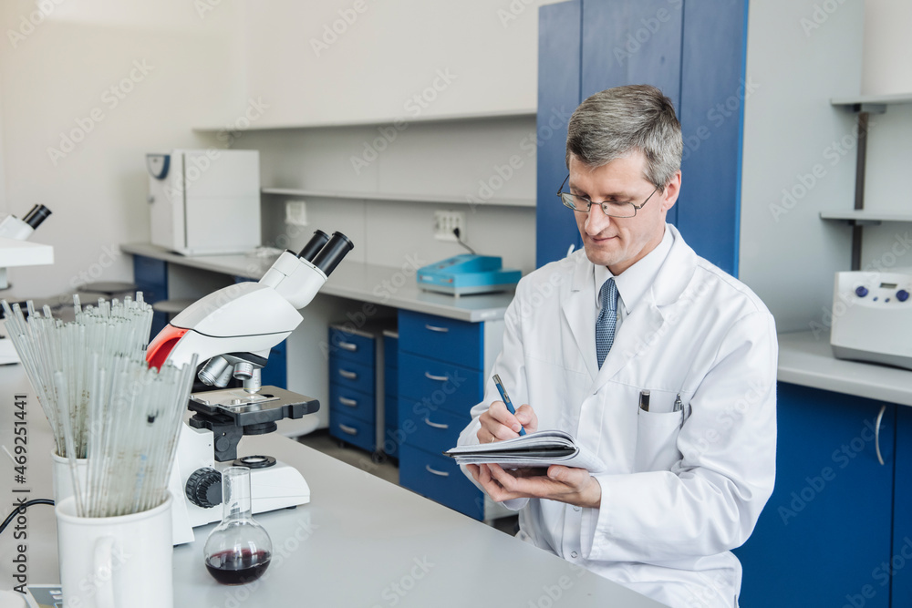 Scientist with eyeglasses writing in note pad at laboratory Scientist with eyeglasses writing in note pad at laboratory