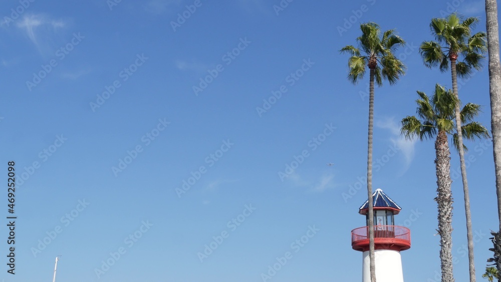 Retro lighthouse, tropical palm trees and blue sky. Red and white vintage old-fashioned beacon. Waterfront fisherman village near ocean sea harbor. Wharf or seaport, sunny summer in California USA.