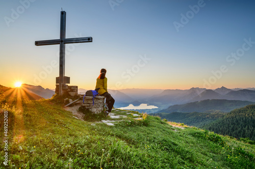 Female hiker sitting by summit cross on mountain peak at sunrise, Carinthia, Austria photo