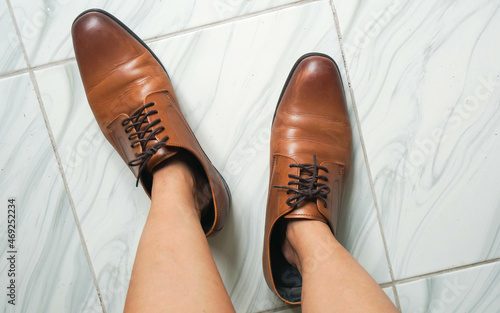 top view  woman feet try to wear oversize brown men leather shoes