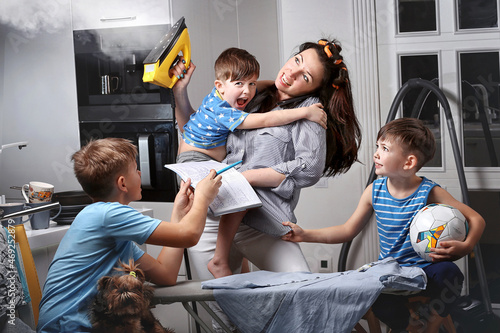 A very busy mother. A very busy woman. A mother who does several things at the same time. A woman who makes several things at the same time. A woman irons and spands time with her children. photo