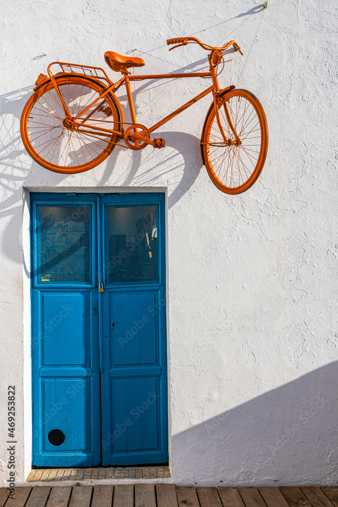 Orange bicycle hanging on a wall above a blue door Orange bicycle hanging on a wall above a blue door