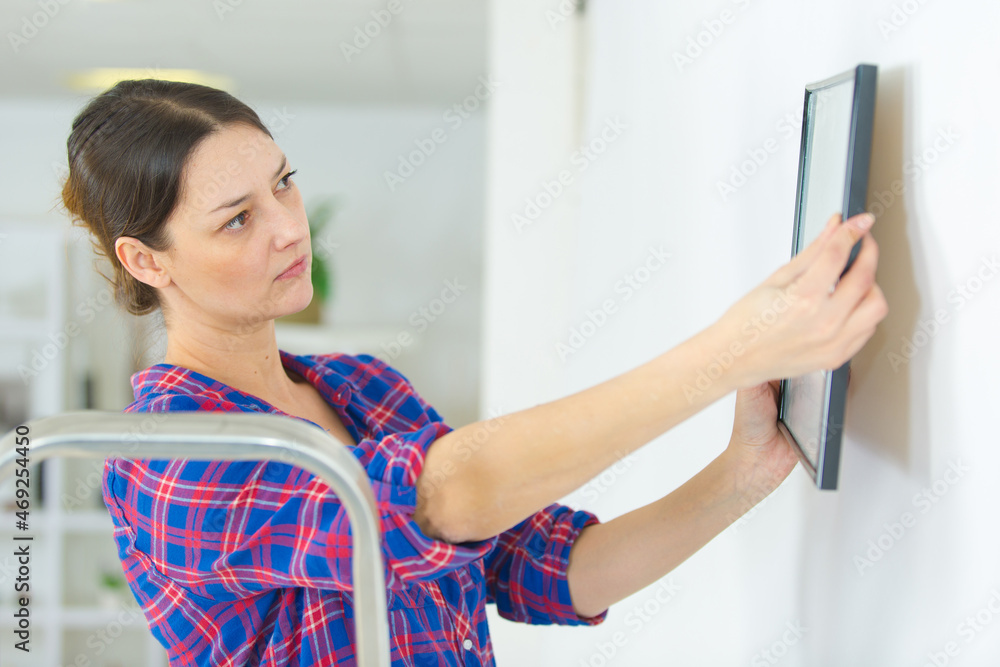 young lady hanging picture on wall young lady hanging picture on wall