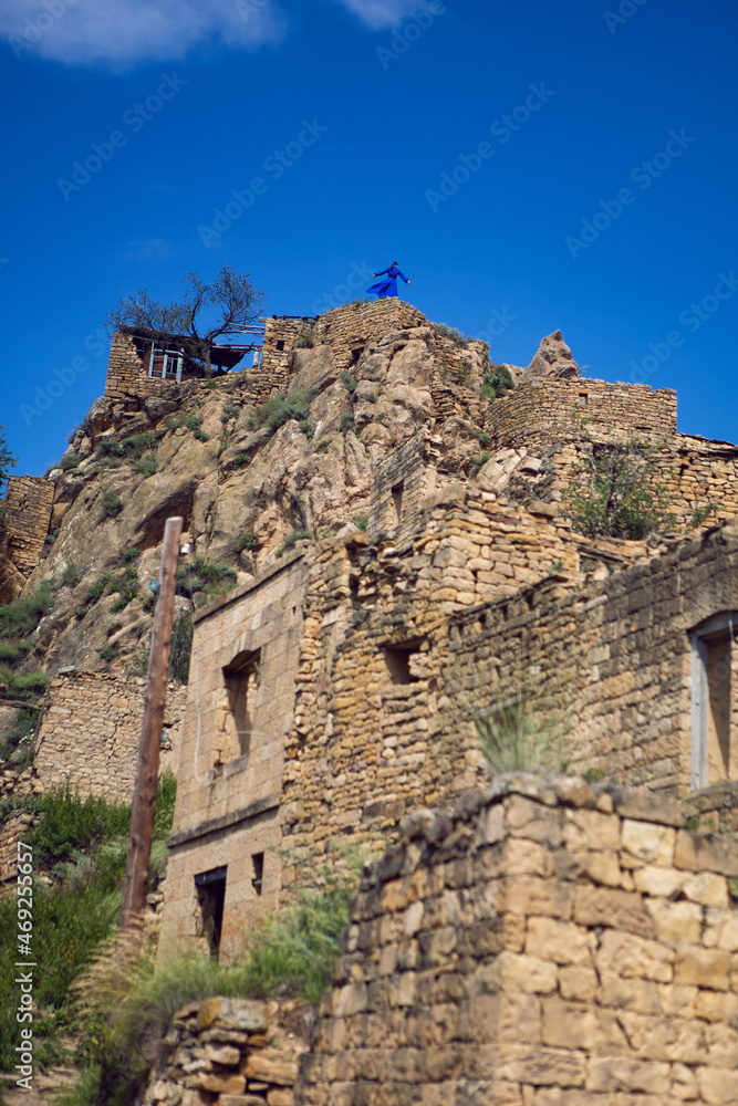 lonely woman in blue dress stands on the very top of the mountain village of gamsutl in Dagestan