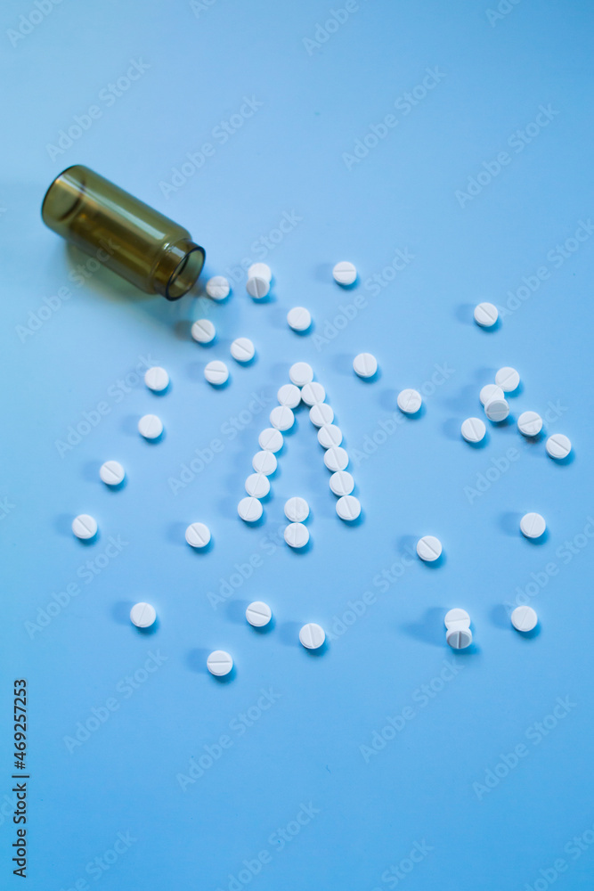 Naklejka premium White medical pills and tablets spilling out of a drug bottle on a blue background. Christmas theme, pills like a Christmas tree. So boxes as an arrow