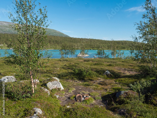 Beatiful camping spot in northern landscape in Swedish Lapland with turquoise blue Vuojatadno river, birch tree forest and green mountains at Padjelantaleden hiking trail. Summer sunny day, blue sky photo