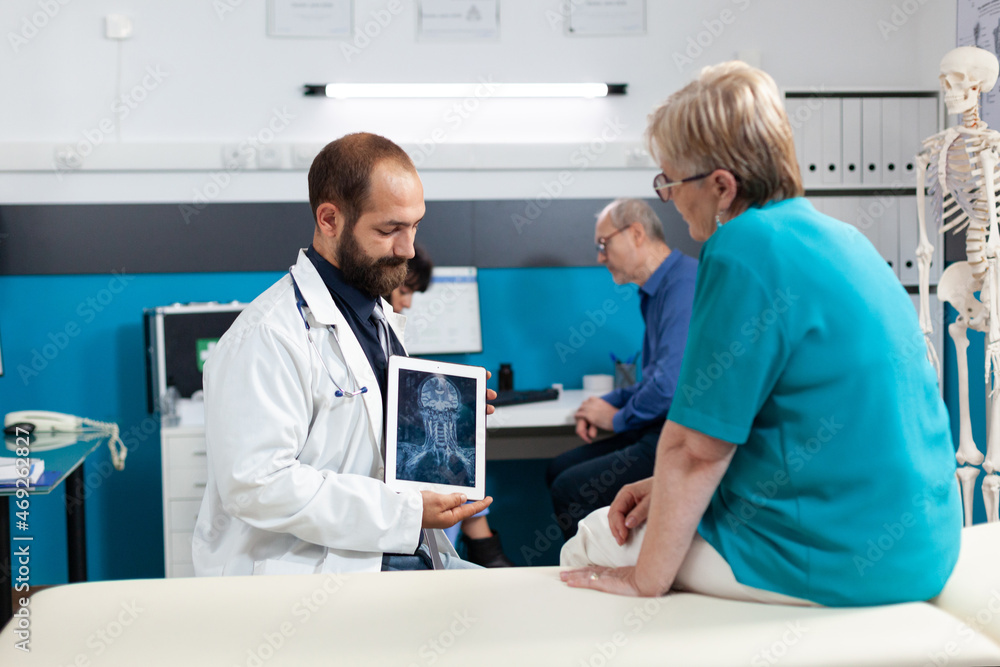 Medic holding tablet with radiography for osteopathy diagnosis in medical office. Retired patient looking at x ray scan on device screen for orthopedic analysis and rehabilitation. Medic holding tablet with radiography for osteopathy diagnosis in medical office. Retired patient looking at x ray scan on device screen for orthopedic analysis and rehabilitation.