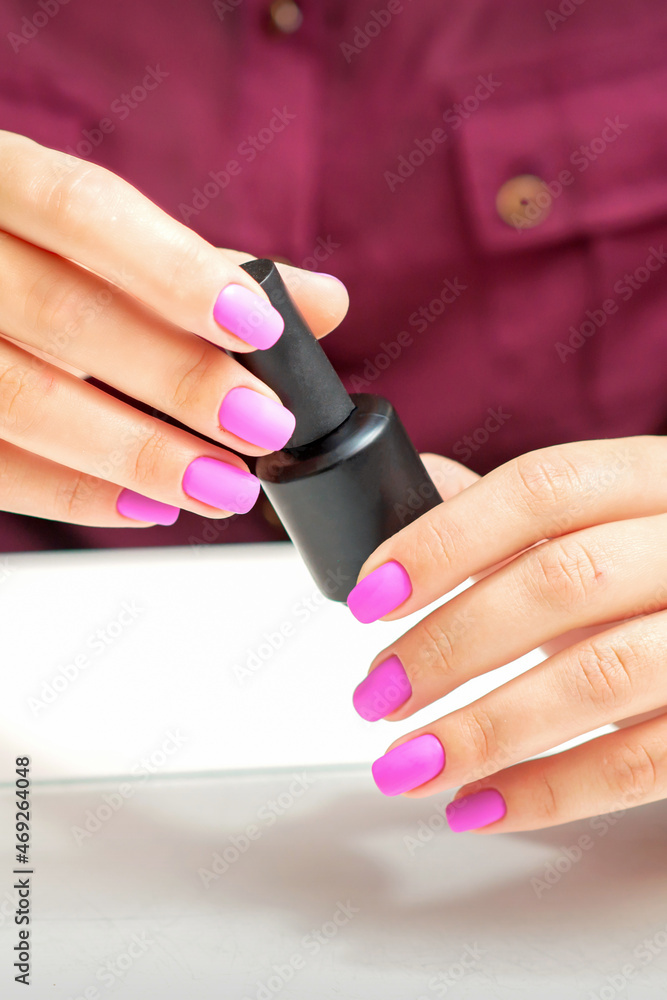 White woman holding nail polish black bottle with painted pink nails close up White woman holding nail polish black bottle with painted pink nails close up