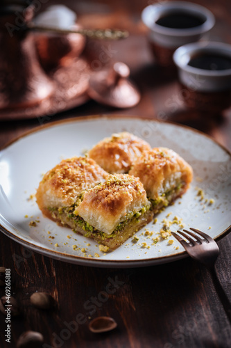 Turkish or Bosnian dessert called Baklava with pistachio served with traditional Turkish or Bosnian coffee set on a wooden board in moody atmosphere © Haris