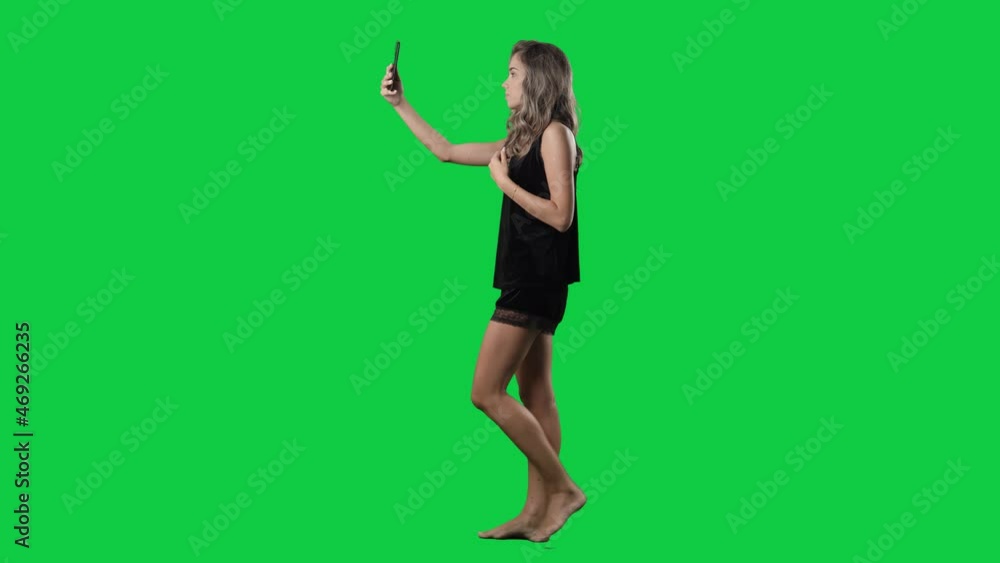 Side view walking woman in pajama taking selfies and sending photos with smartphone. Full body isolated on green screen background Side view walking woman in pajama taking selfies and sending photos with smartphone. Full body isolated on green screen background
