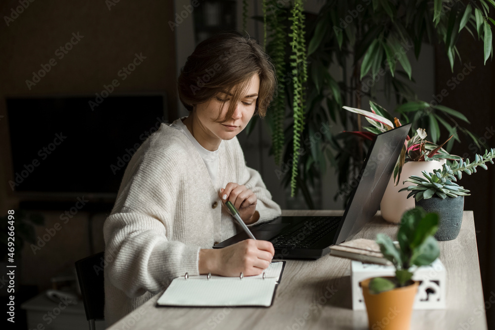 Freelancer with laptop writing in book at table Freelancer with laptop writing in book at table