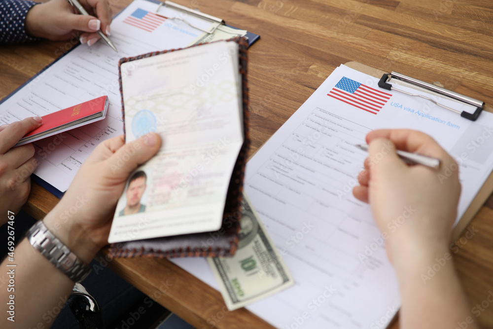 People filling visa application forms with personal passports at embassy