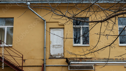 Old white wooden door to nowhere on the background of the old yellow wall with windows.