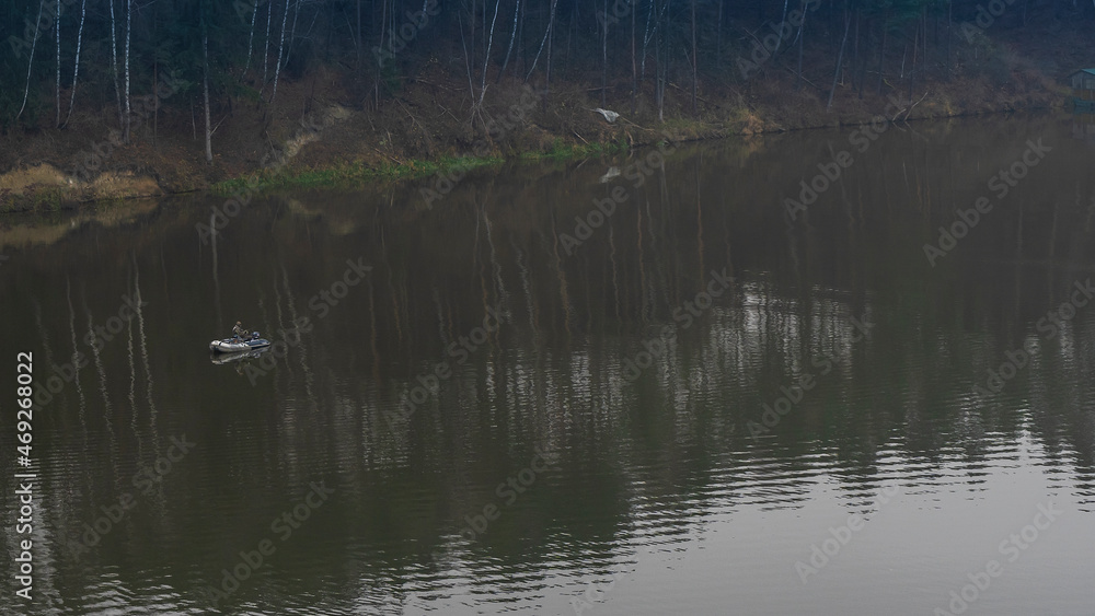 Fisherman in rubber boat on the river. Mature man fishing from the boat on the river at evening. Fisherman in rubber boat on the river. Mature man fishing from the boat on the river at evening.