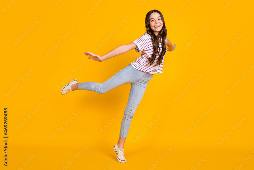 Full size profile side photo of young girl happy positive smile have fun hands wings plane isolated over yellow color background Full size profile side photo of young girl happy positive smile have fun hands wings plane isolated over yellow color background