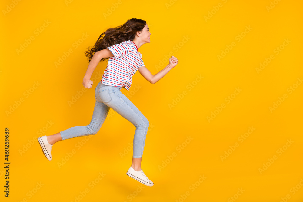 Full size profile side photo of young girl jump up go walk run hurry sale look empty space isolated over yellow color background Full size profile side photo of young girl jump up go walk run hurry sale look empty space isolated over yellow color background