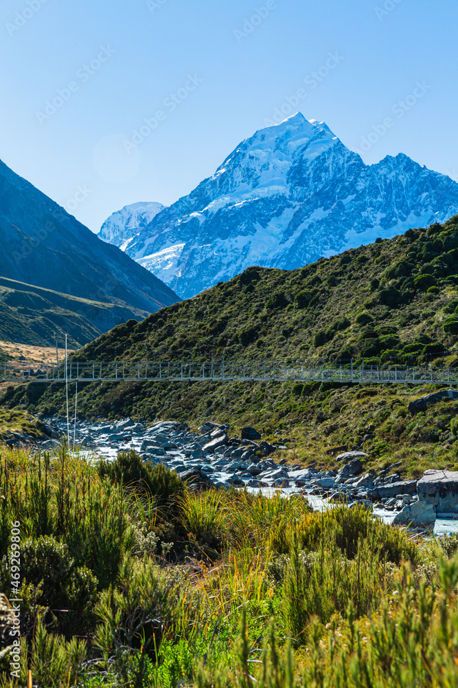 Obraz premium ニュージーランド アオラキ・マウント・クック国立公園のフッカー・バレー・トラックのトレッキングコースにある第三の吊り橋と後ろにそびえる南アルプス山脈のアオラキ山