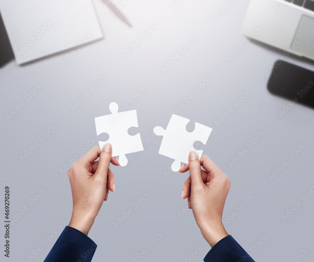 Hands holding a jigsaw puzzle piece at on white office desk table top view with copy space for teamwork concept. Hands holding a jigsaw puzzle piece at on white office desk table top view with copy space for teamwork concept.