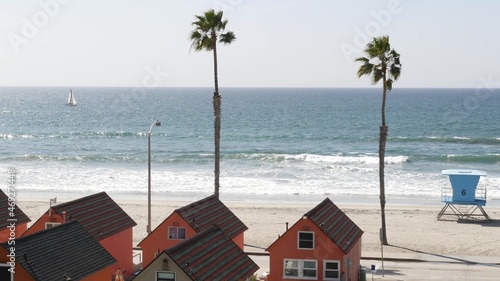 Colorful waterfront cottages  Oceanside California USA. Multicolor bungalow huts  summer sea  beachfront lodging. Many vacation houses on beach  ocean waves and palm trees. Lifeguard tower  watchtower