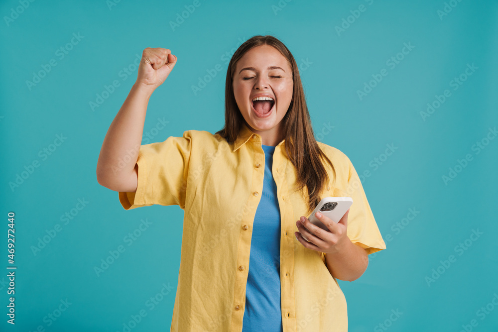 Young white woman making winner gesture while using cellphone Young white woman making winner gesture while using cellphone
