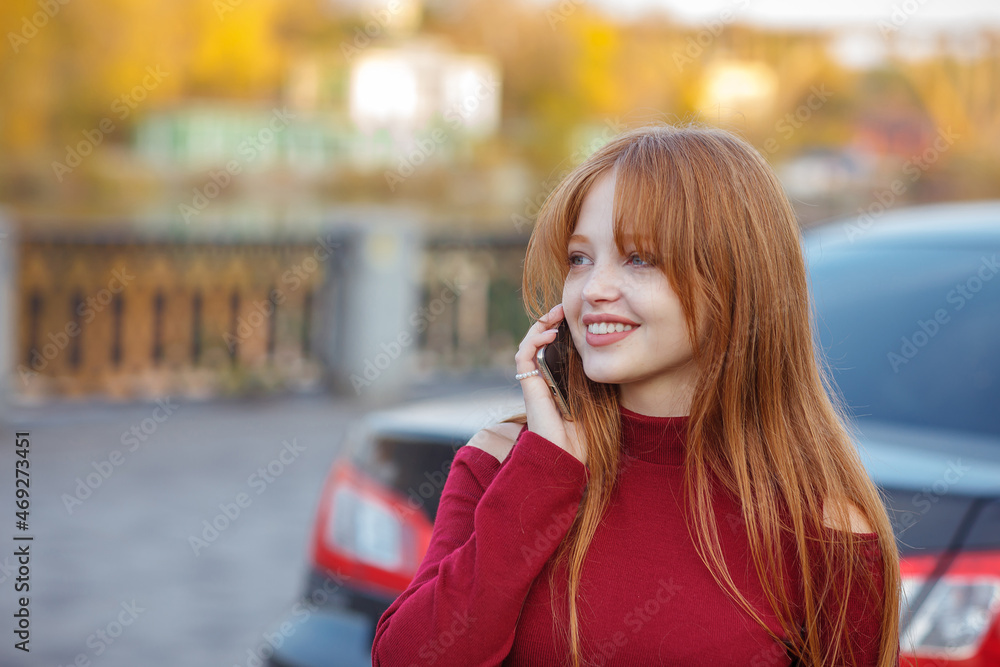 Portrait casual of a Red hair girl in a red dress, looking a straight and smiles, speaking on a phone. stays on a street. model beautiful, long straight hair, copy space. Blurred details