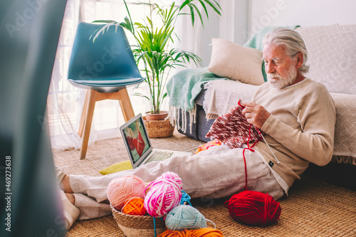 Senior man learning to knit wool through laptop at home photo