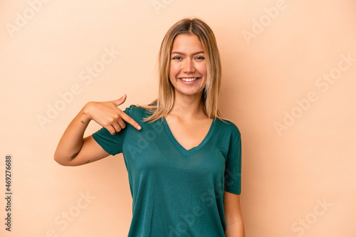 Young caucasian woman isolated on beige background person pointing by hand to a shirt copy space, proud and confident