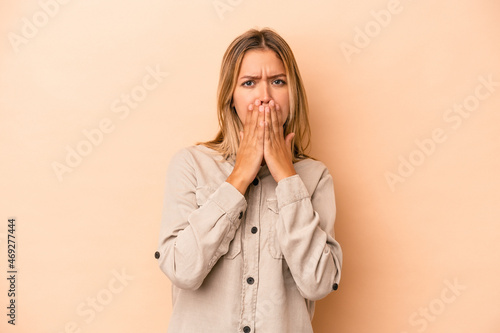 Young caucasian woman isolated on beige background covering mouth with hands looking worried.