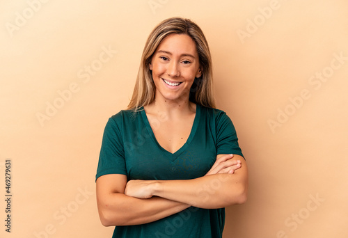 Young caucasian woman isolated on beige background who feels confident, crossing arms with determination.