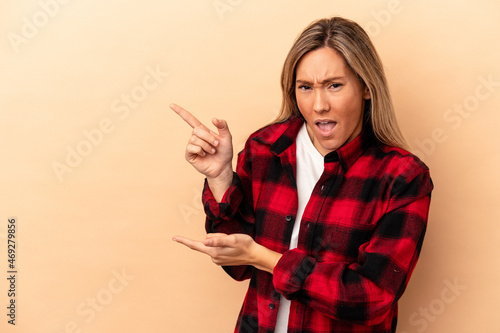 Young caucasian woman isolated on beige background pointing with forefingers to a copy space, expressing excitement and desire.