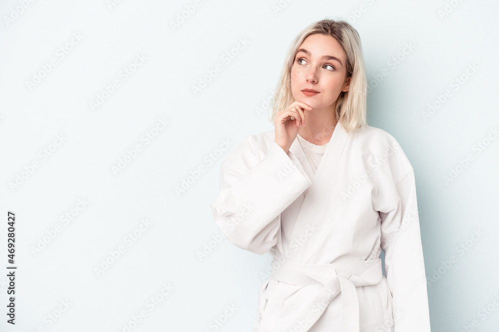 Young caucasian woman doing karate isolated on blue background looking sideways with doubtful and skeptical expression. Young caucasian woman doing karate isolated on blue background looking sideways with doubtful and skeptical expression.