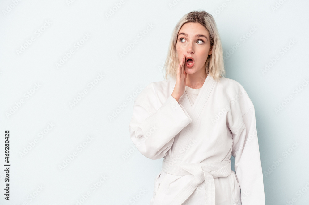 Young caucasian woman doing karate isolated on blue background is saying a secret hot braking news and looking aside Young caucasian woman doing karate isolated on blue background is saying a secret hot braking news and looking aside