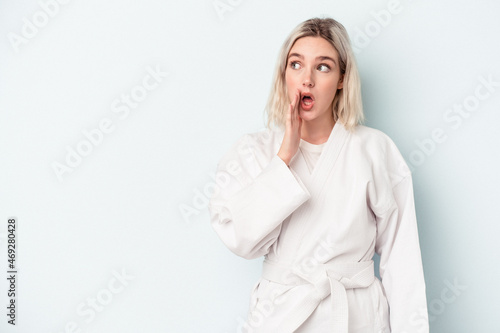 Young caucasian woman doing karate isolated on blue background is saying a secret hot braking news and looking aside © Asier