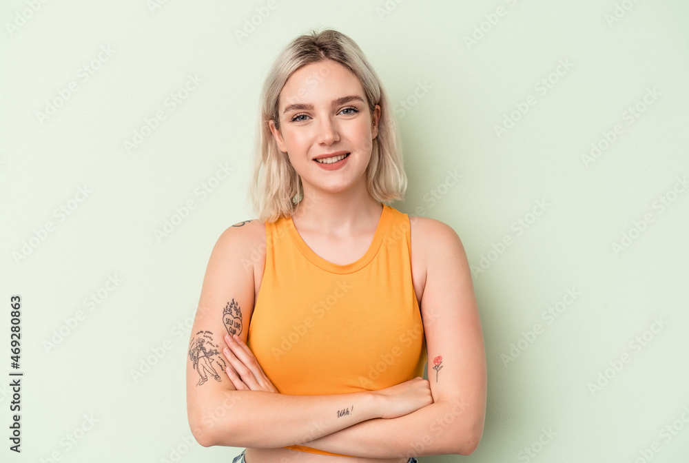 Young caucasian woman isolated on green background who feels confident, crossing arms with determination.