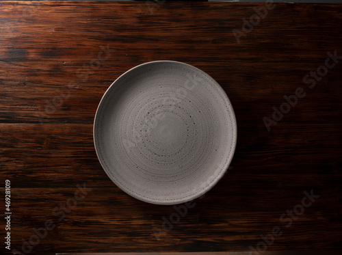 Plato redondo beige vacío sobre tabla de madera. Vista cenital. Round empty beige plate on wooden board. Zenithal view.