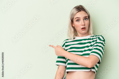 Young caucasian woman isolated on green background smiling and pointing aside, showing something at blank space.