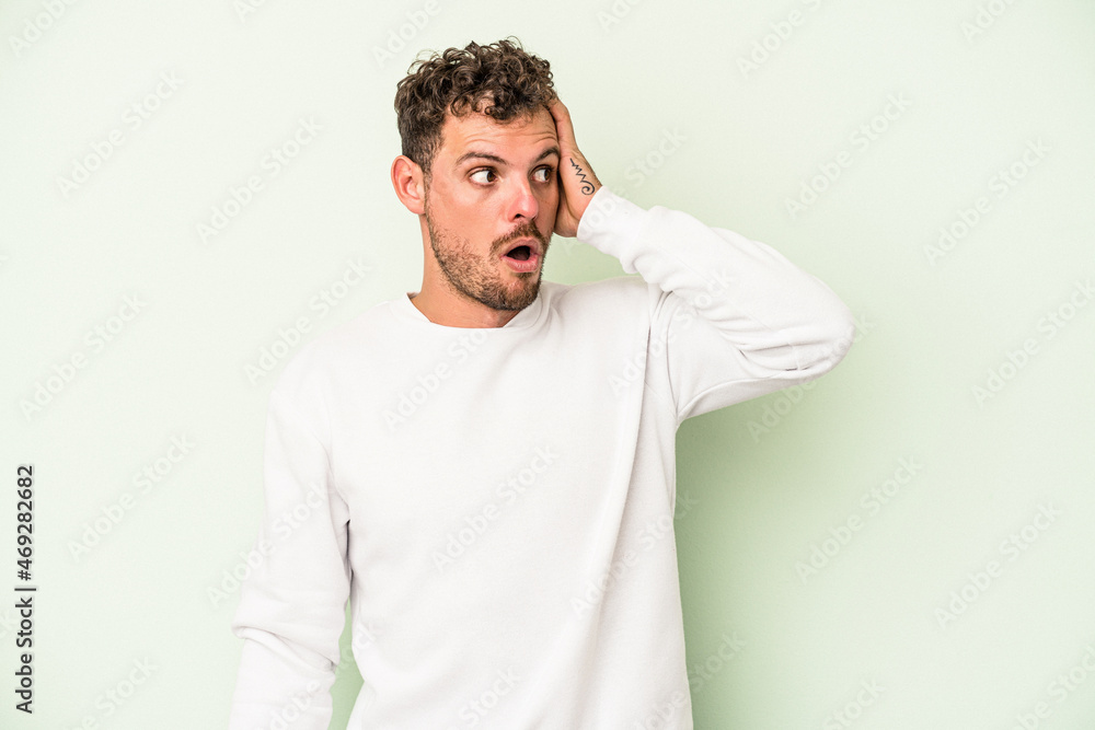 Young caucasian man isolated on green background being shocked, she has remembered important meeting.