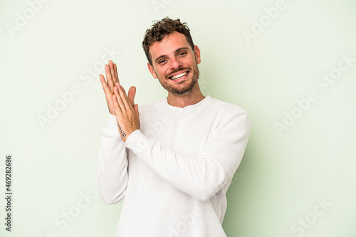 Obraz na plátně Young caucasian man isolated on green background feeling energetic and comfortable, rubbing hands confident