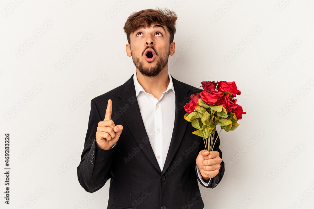 Young mixed race man holding bouquet of roses isolated on white background pointing upside with opened mouth. Young mixed race man holding bouquet of roses isolated on white background pointing upside with opened mouth.