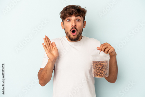 Canvas Print Young mixed race man holding a birds food isolated on blue background surprised and shocked
