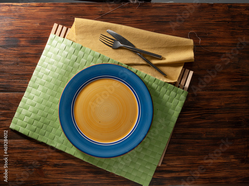 Plato cenital amarillo y azul con cubiertos y sobre tabla de madera. Yellow and blue zenith plate with cutlery and on wooden table.