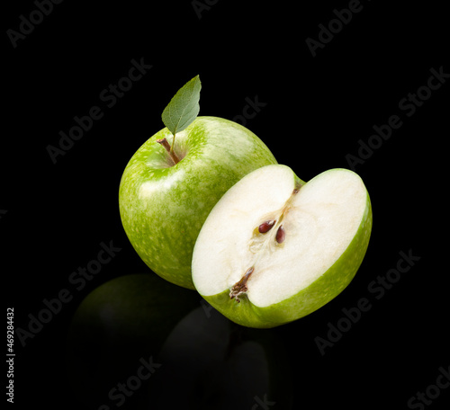 Manzana verde entera y cortada con hoja sobre fondo negro. Whole and cut green apple with leaf on black background.