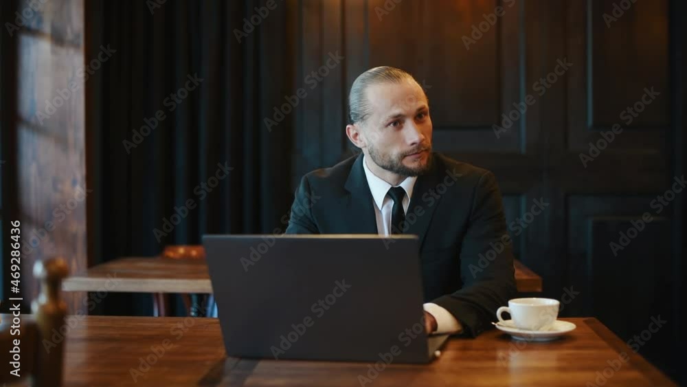 Young stylish businessman in formal clothes sits indoors with laptop and closing it Young stylish businessman in formal clothes sits indoors with laptop and closing it