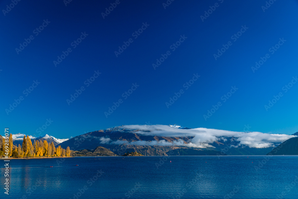 ニュージーランド　オタゴ地方のワナカ湖の湖畔の紅葉で黄色に染まった木々と南アルプス山脈のアルタ山