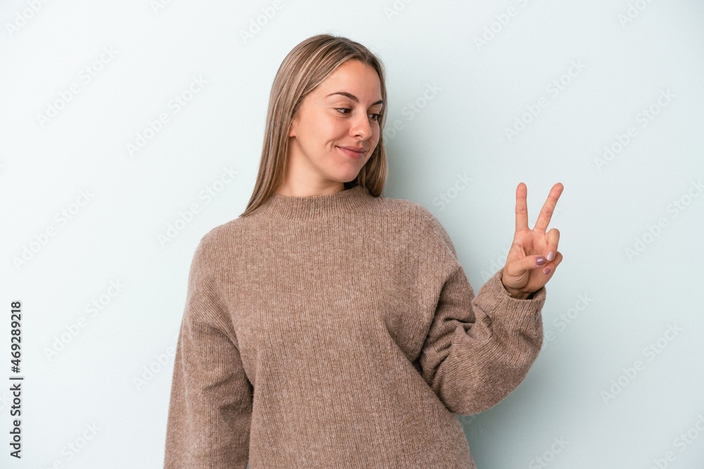 Young caucasian woman isolated on blue background joyful and carefree showing a peace symbol with fingers. Young caucasian woman isolated on blue background joyful and carefree showing a peace symbol with fingers.