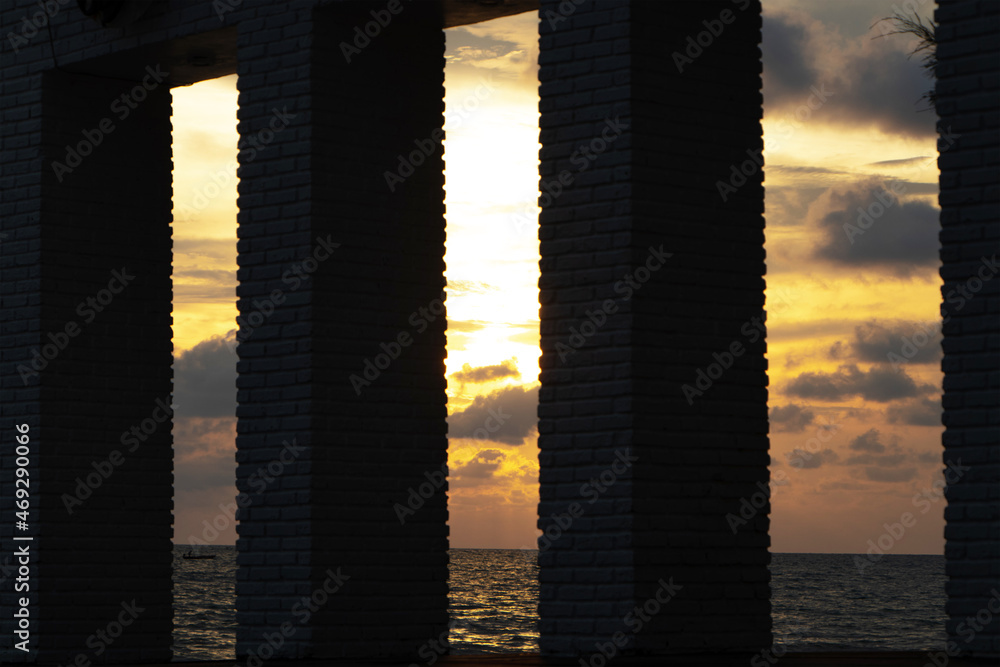 View of the Thai Sea during sunset, at low tide. A colorful dramatic orange sky. The sunset is shadowed between three concrete pillars with beautiful colors in the evening.
