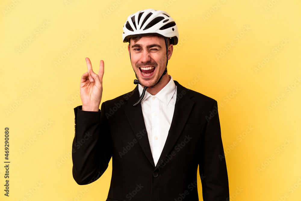 Young caucasian business man wearing a bike helmet isolated on yellow background joyful and carefree showing a peace symbol with fingers. Young caucasian business man wearing a bike helmet isolated on yellow background joyful and carefree showing a peace symbol with fingers.